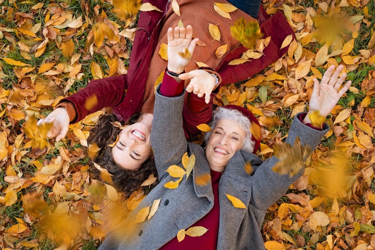 Two women laying down and playing in the orange Fall leaves