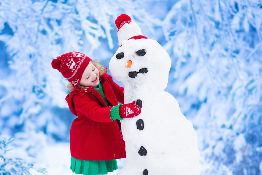 Child wearing red coat and hat making a snowman