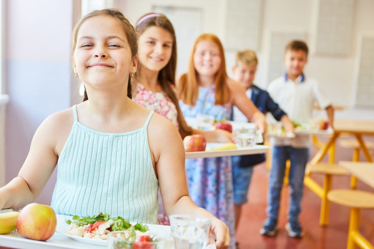 Row of children holding lunch trays in their school cafeteria