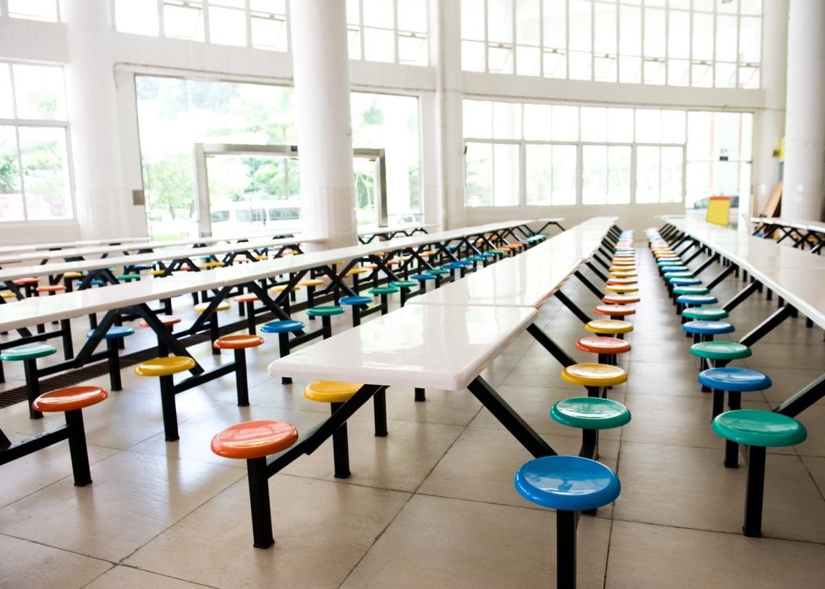 Empty school cafeteria with long tables and colorful seats