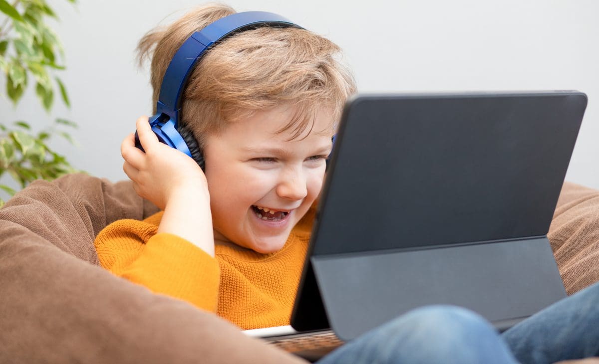 Child wearing headphones laughs while watching a video on a tablet