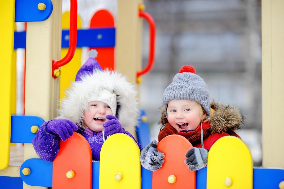 Two kids in winter coats play on a colorful playground