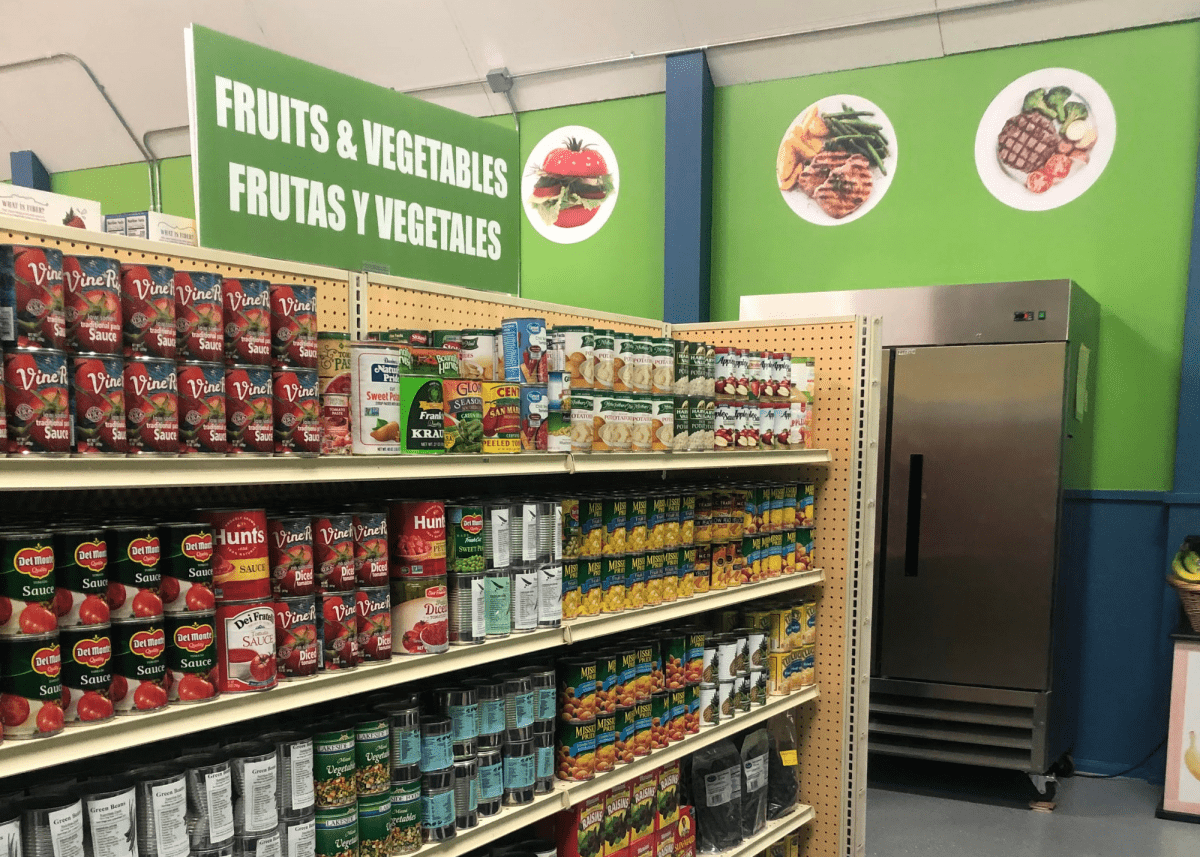 Shelf at a food pantry with a sign that says "Fruits & Vegetables" in both English and Spanish