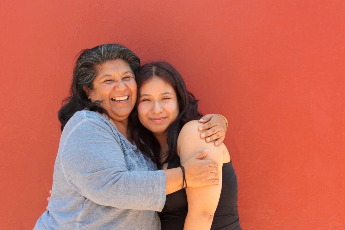Smiling mother and daughter standing in front of a neutral background