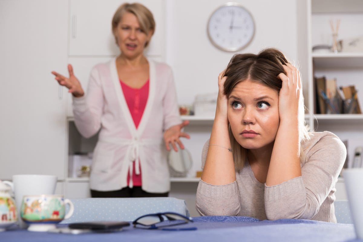 Frustrated teenage girl sitting at table with her head in her hands while her mom asks her about her weight