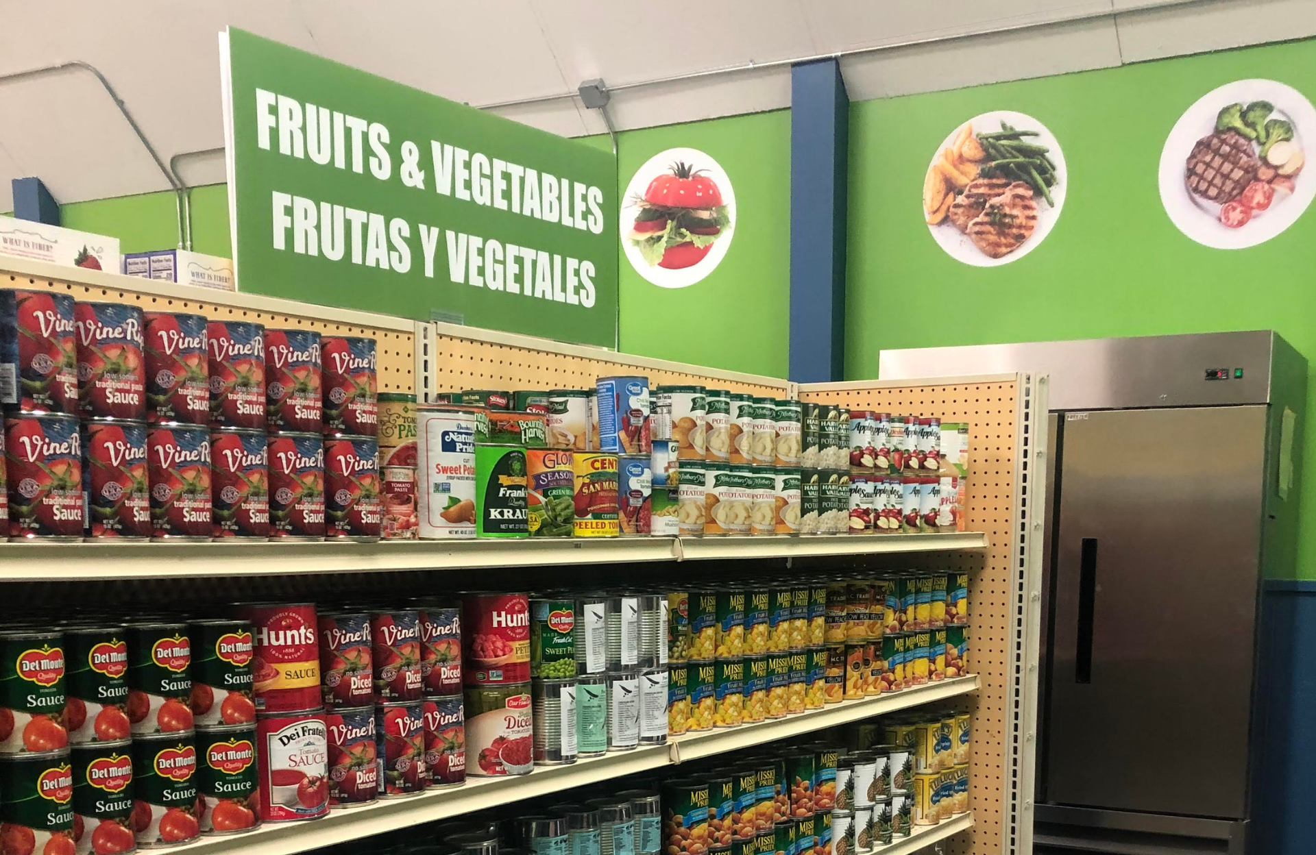 Shelf at a food pantry with canned produce. A sign says 